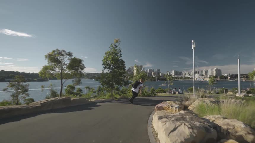 A man rollerblading in a park pathway close to the coast with a bridge in the foreground