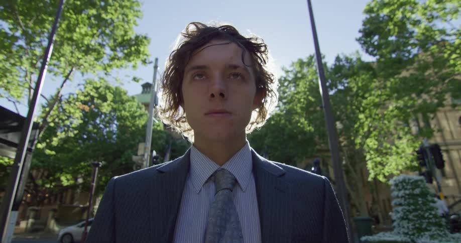 A man in a suit and tie stands outside as traffic passes by behind him