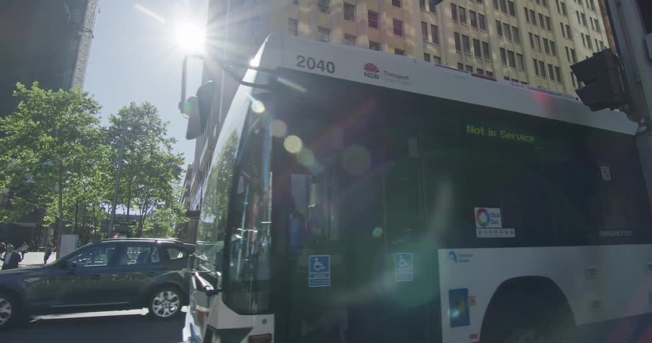 A city bus driving with people and buildings in the background
