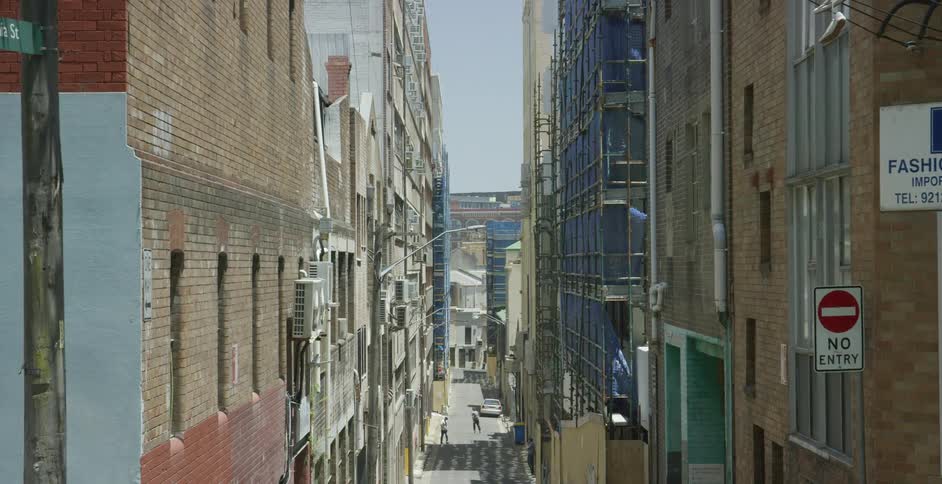 A person skates down a street as others walk by and a car drives by