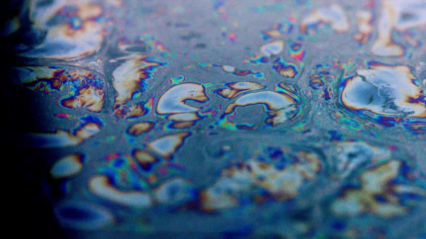 Color swirls on surface of liquid contrast with blackness