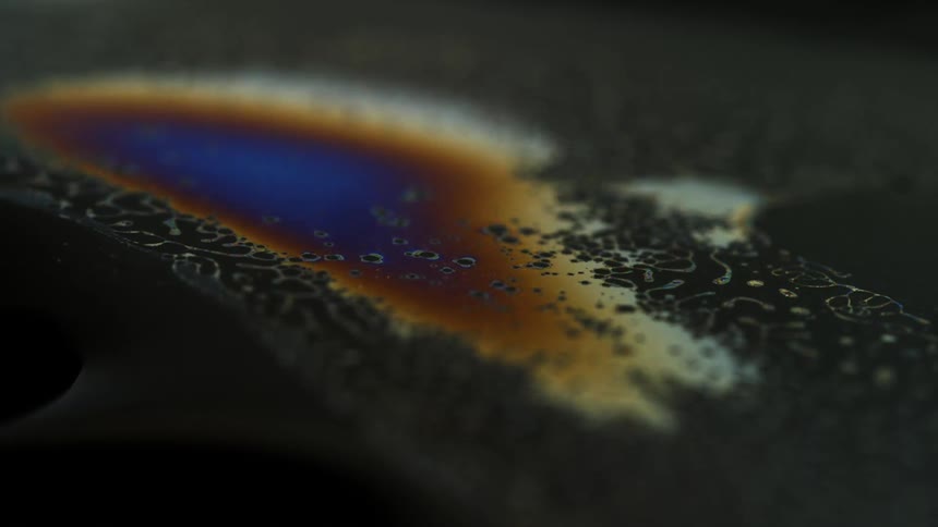 Oil breaks liquid surface with colorful patterns