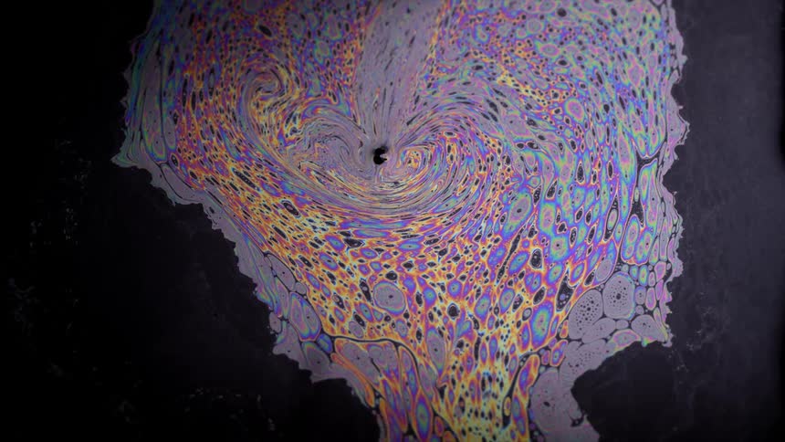 Colors swirl and float on the surface of dark liquid