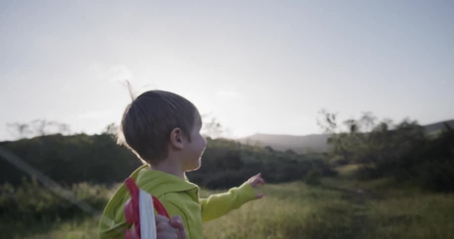 A boy holds the handle of a kite and runs through a field with a large smile on his face