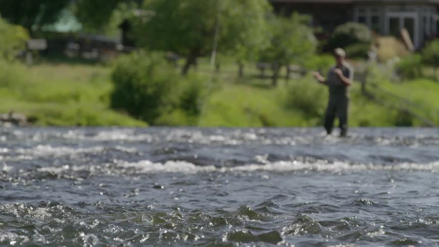 Blurry view of a man fishing in a river with rough waves in the foreground
