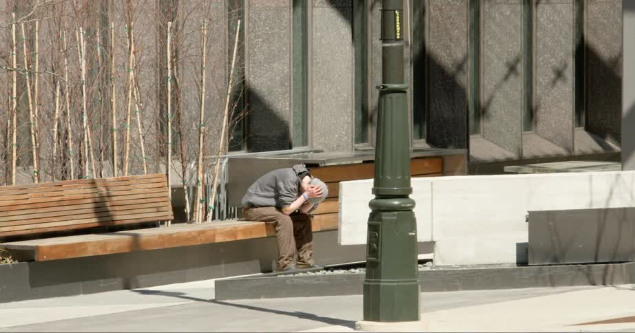 A teenager sits outside on a bench with his head hung low and resting in his hands