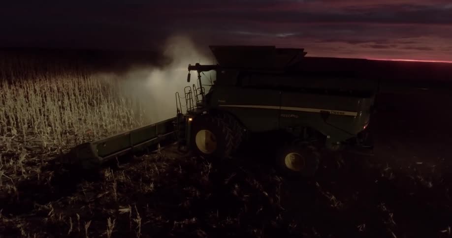 A tractor with a thresher and a spotlight moves through a farm field