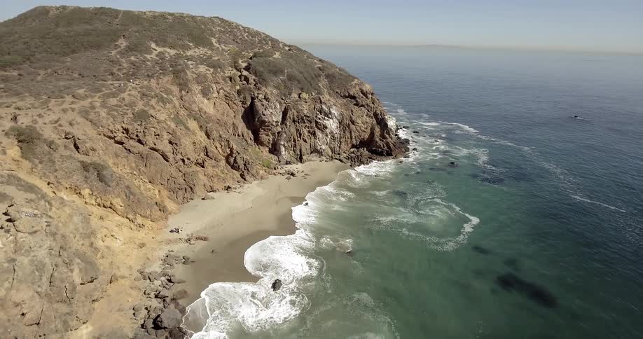 A sandy beach by a rocky coast with a person walking on the beach