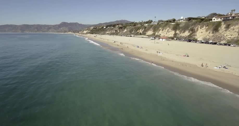 A beach with sand and people with mountains in the background