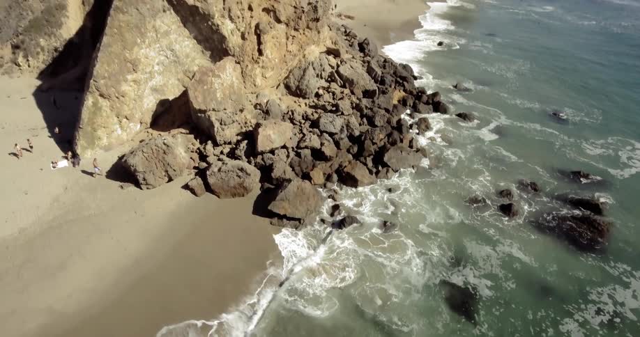 People walk around the beach and climb promontory as waves crash on the beach