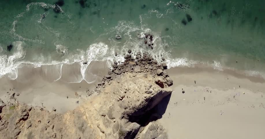Aerial view of ocean waves crashing against the shore on a sunny day