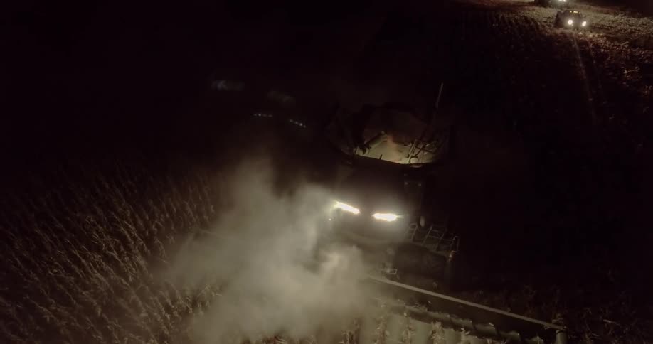 A combine harvester cuts down and harvests rows of crops at night
