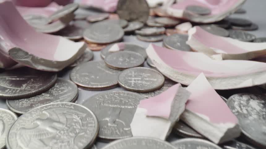 Coins and broken pieces of piggy bank lie on a gray surface