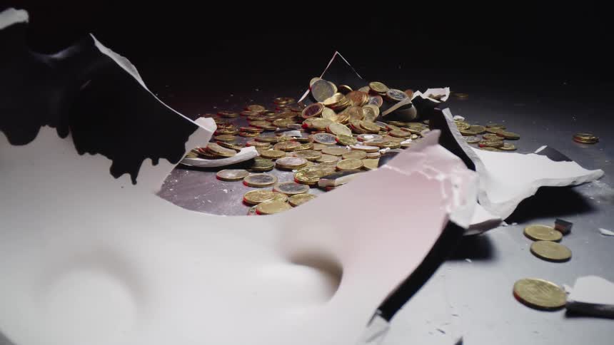 A pile of coins is surrounded by broken pieces of a ceramic piggy bank