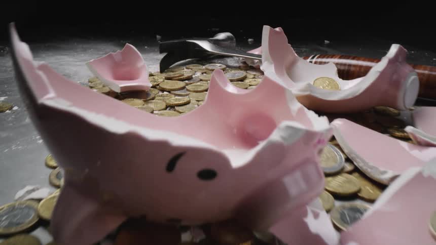 Pink piggy bag shattered by a hammer laying in a pile of coins
