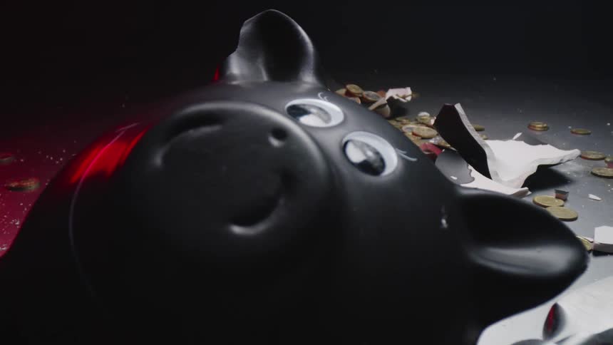 A broken black piggy bank with a hammer with coin scattered everywhere