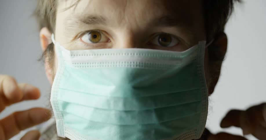 A white man puts a mask on over his mouth and nose