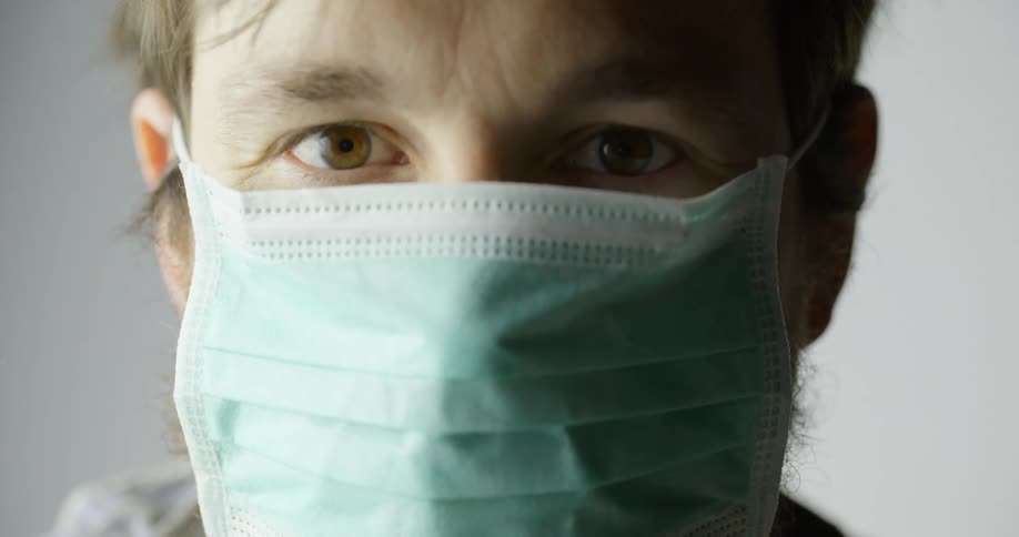 A man holds up a disposable mask and then puts it on covering his nose and mouth