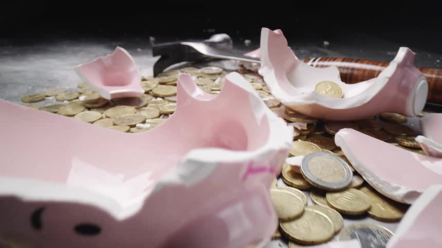 A hammer and money sit in the remains of a piggy bank