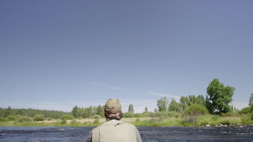 A man fly fishing in a wide river on a sunny day