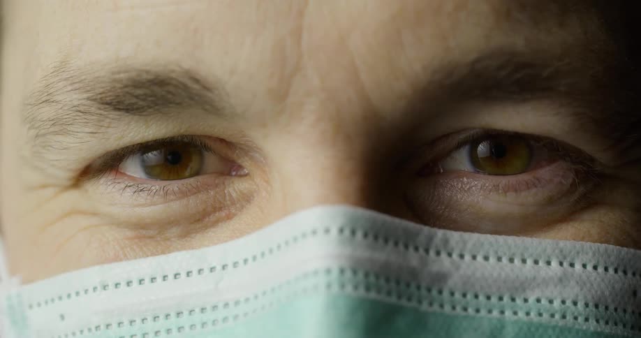 A white man wearing a mask blinks his eyes