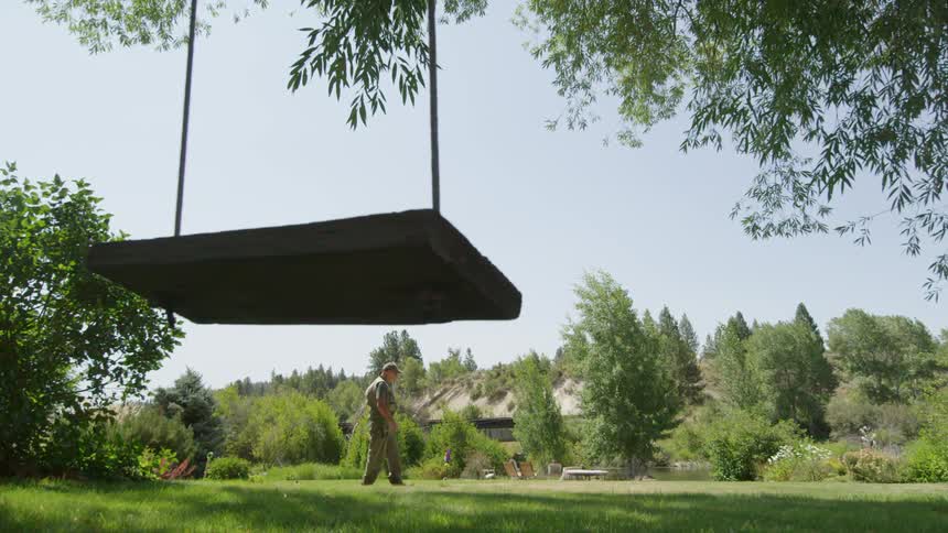 A man carrying a fishing pole walks past a backyard swing