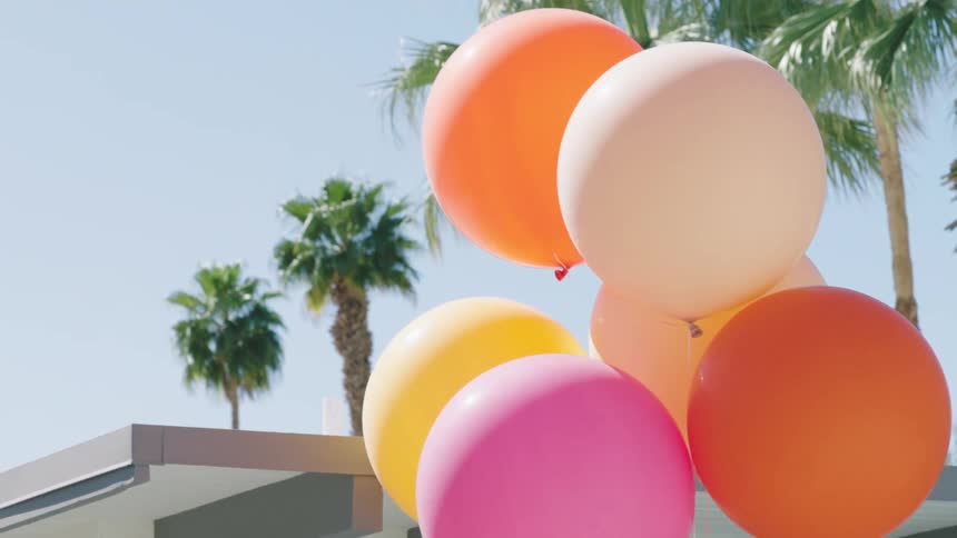 Colorful balloons are tied outside a house in a tropical town with palm trees