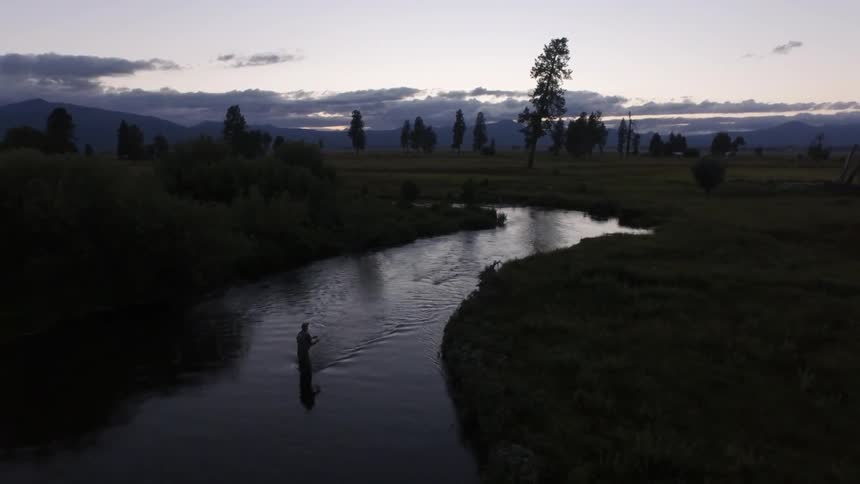 A person fly fishing in a river at dusk