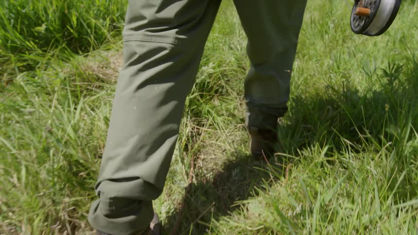 A fisherman walks through tall grass