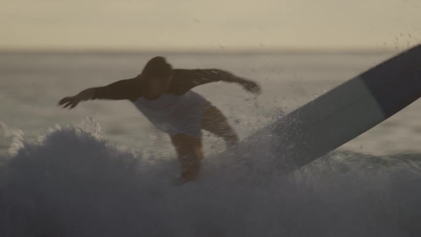 A young, long-haired man surfing before eventually falling into the water