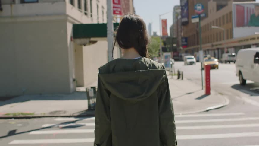 A woman carrying a bag and drink crossing a street in a metropolis