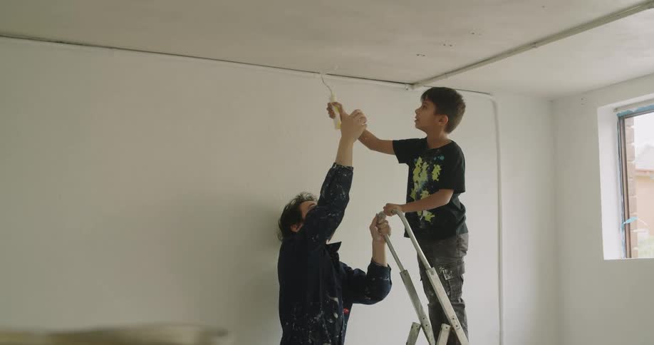 A man helps the boy paint the ceiling