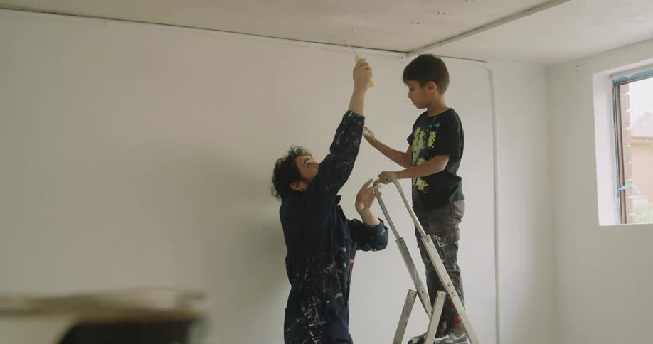 Father teaches son how to use roller to paint ceiling