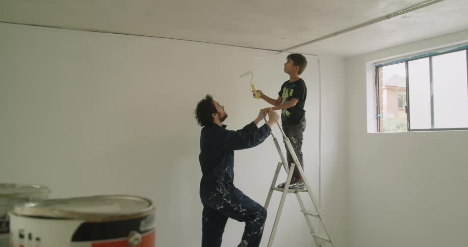 A man gives a paint roller to a child and shows him how to paint