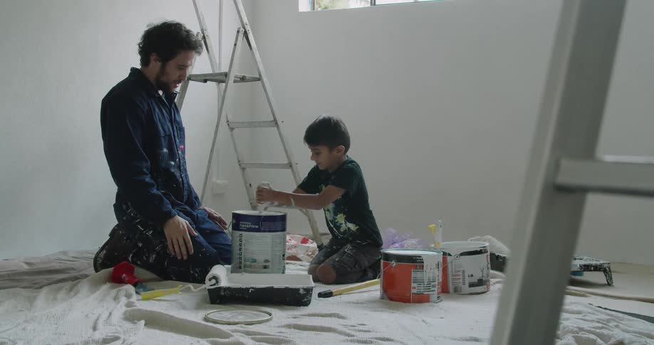A child stirring a can of paint as a man watches over him