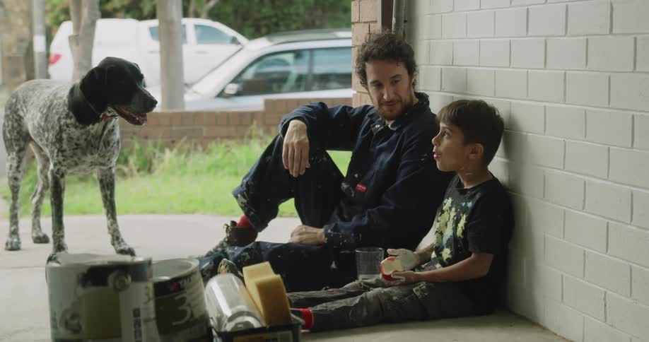 Father and son sitting and resting against a wall talk to each other during break