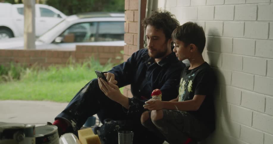 A father uses his phone as a child eats outside
