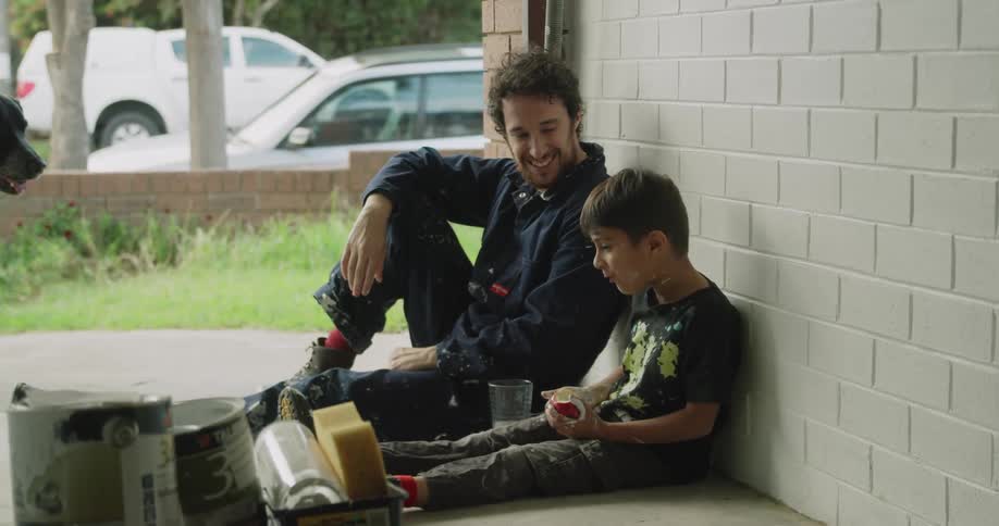 A dad tickles and teases his son while they take a lunch break from painting