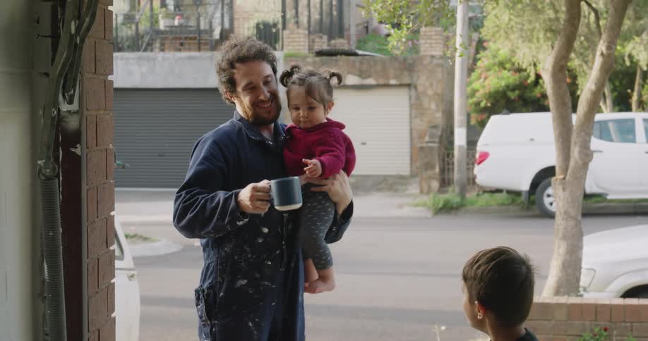 A man holds his daughter and drinks from a mug as a child plays with a dog