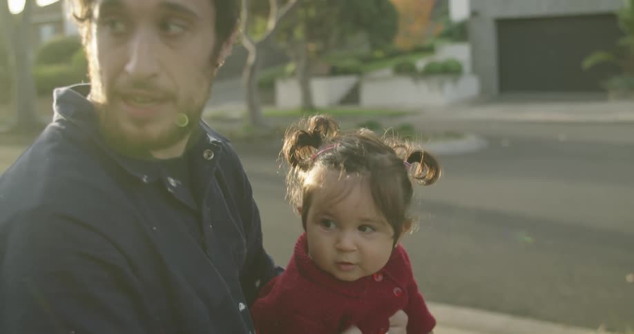 A man holds his daughter in his lap as they sit outdoors in their front lawn