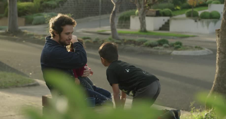 A man holds his daughter as he watches his son play in their front lawn
