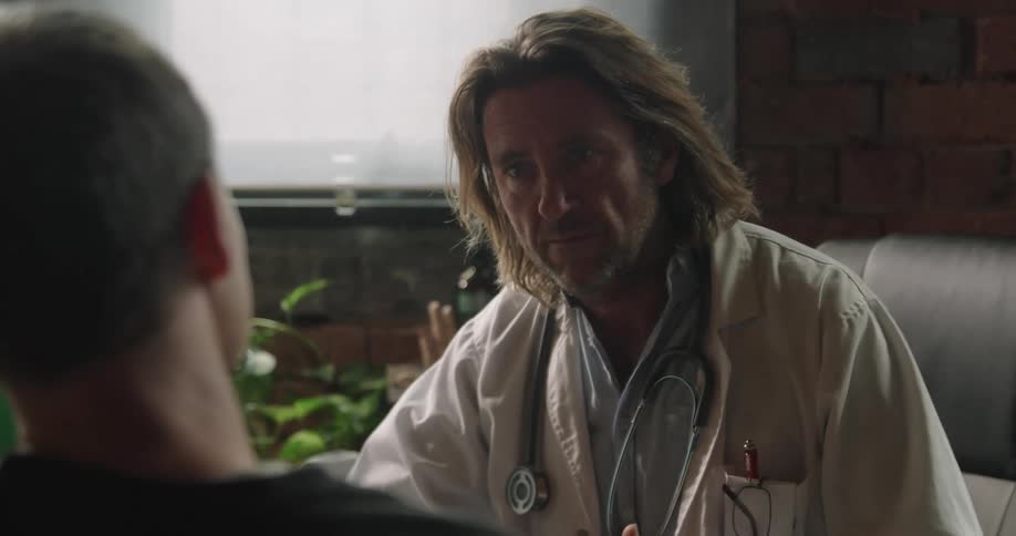 A doctor in a white coat speaks with a patient in an office