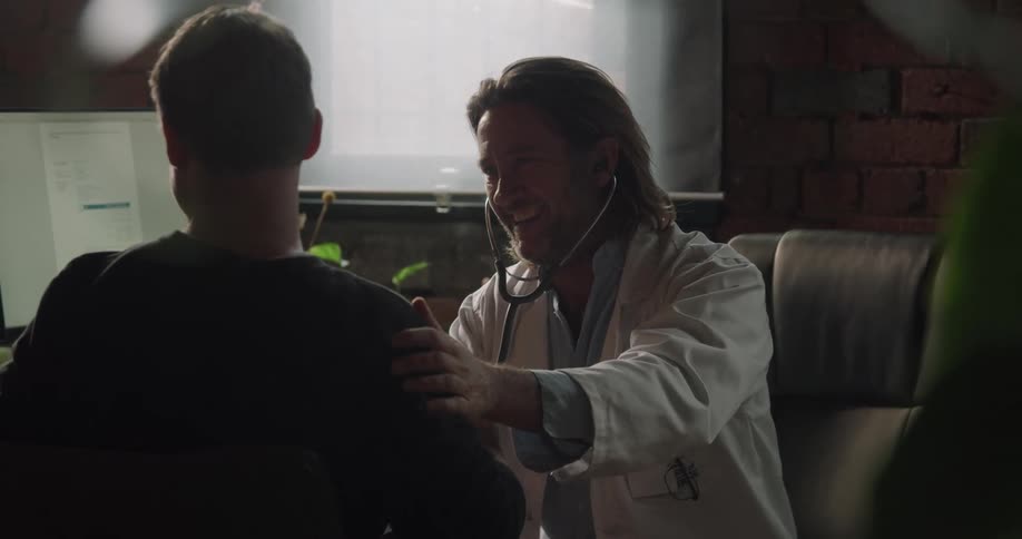 A doctor smiles and nods as he listens to a patients lungs with a stethoscope in his office