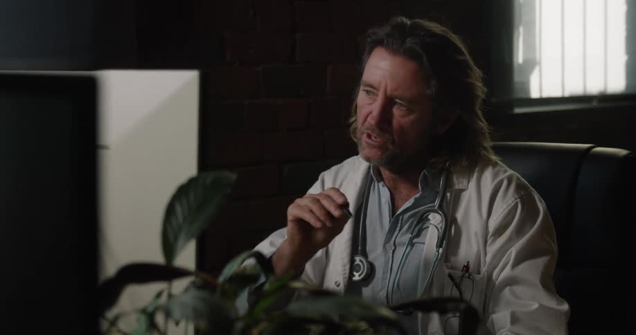 A doctor sitting at his desk talking and gesturing into the monitor