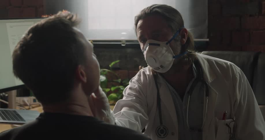 A doctor wearing a mask touches a mans face as he examines a patient in his office