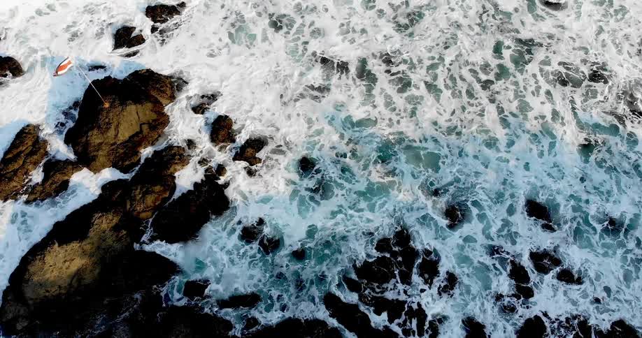 A flagpole is planted on a rock along the shore of the ocean