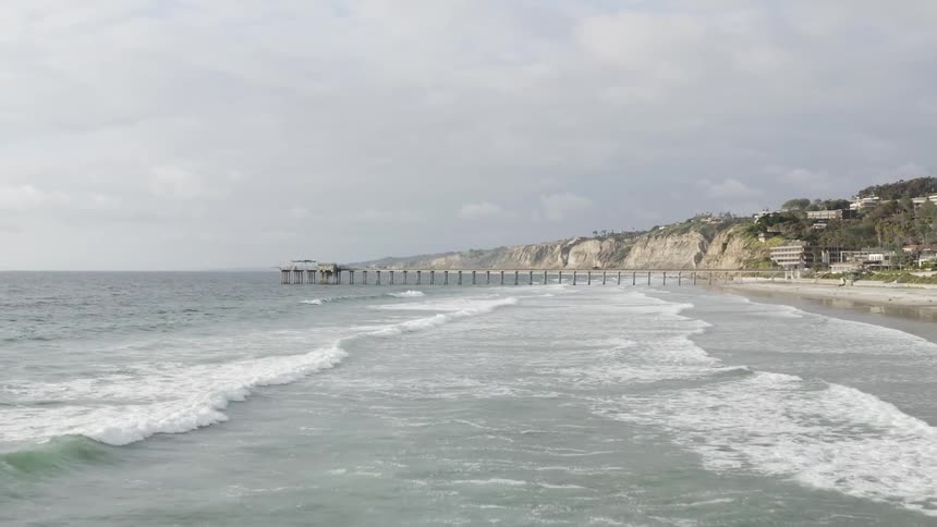 Ocean waves come to shore on an empty beach and a long pier