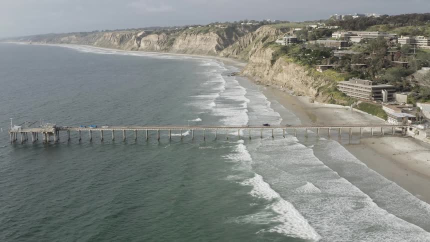 A pier jutting out into the ocean from a beach next to a small city
