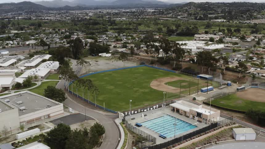 Sports fields and pool stand empty in the middle of a sprawling city bordered by mountains
