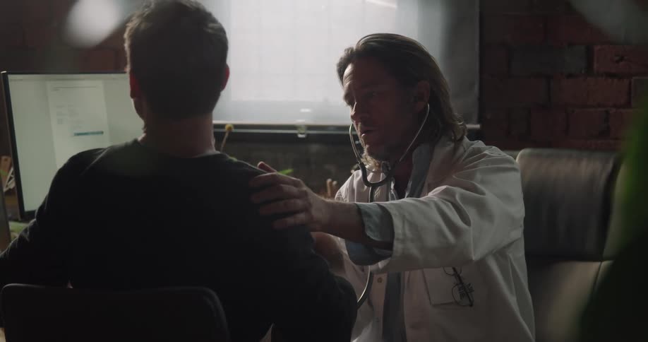 A male doctor checks a patients breathing in his office